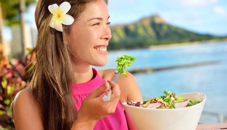 Salad eating healthy woman at restaurant in Hawaii. Asian Multiracial young female adult sitting at beach cafe eating a vegetarian lunch meal during summer vacations in Waikiki, Honolulu, Hawaii, USA.